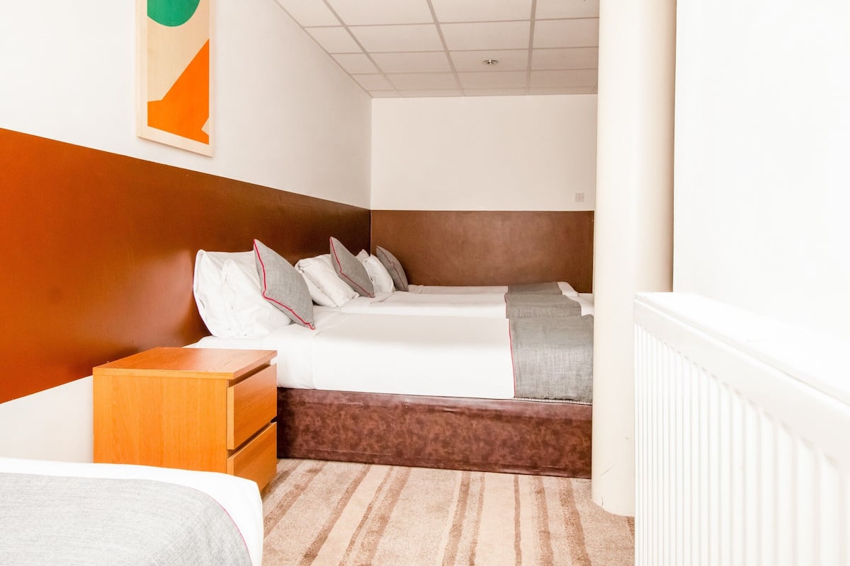 A hotel room with a bed, a wooden nightstand, a headboard, and a radiator.