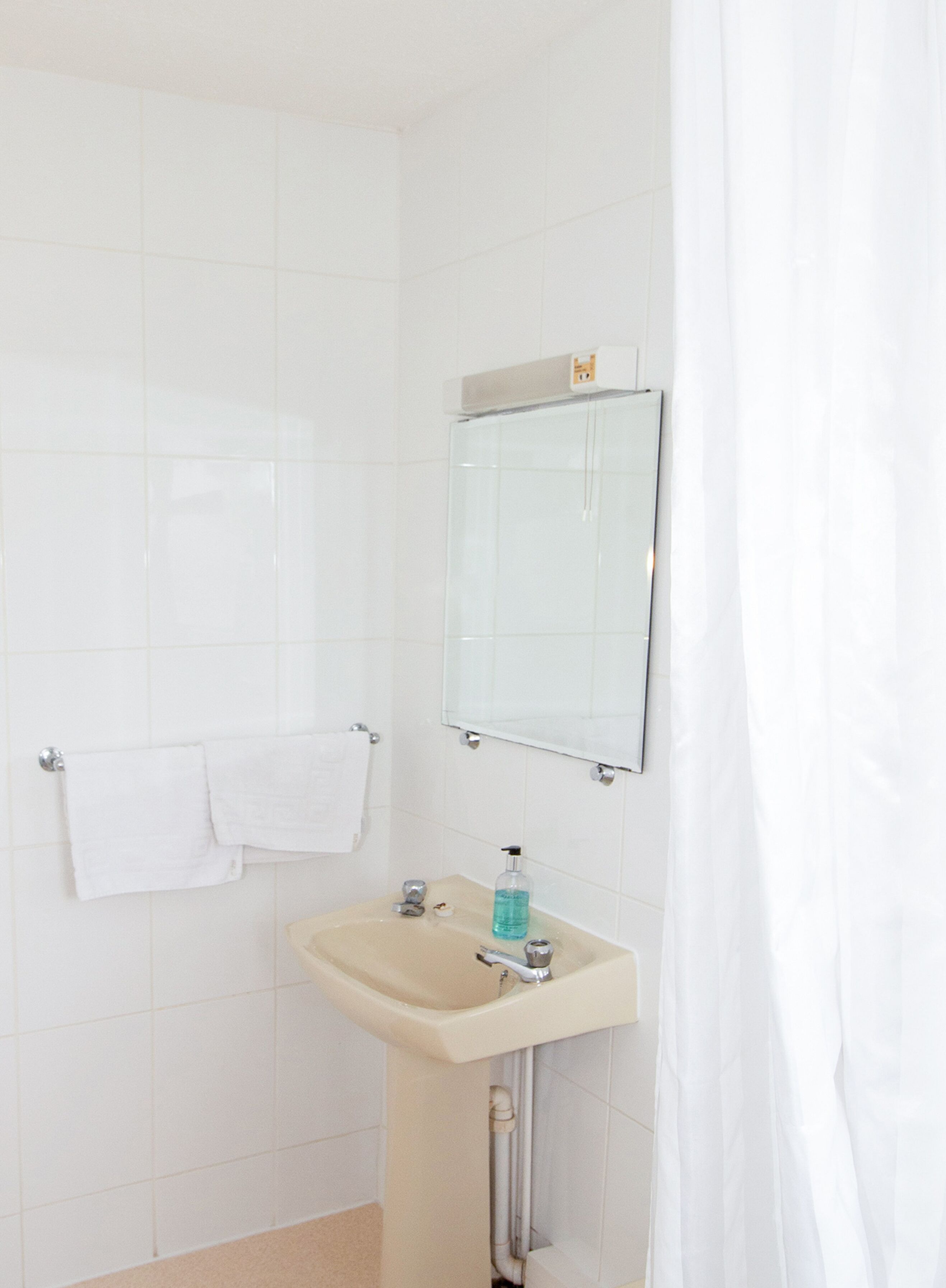 A bathroom with white tiles, a sink, a mirror, and a towel rack.