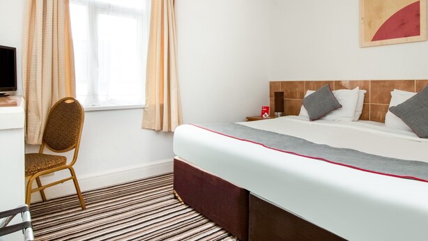 Una habitación de hotel con cama, una silla, un escritorio y una ventana con cortinas.