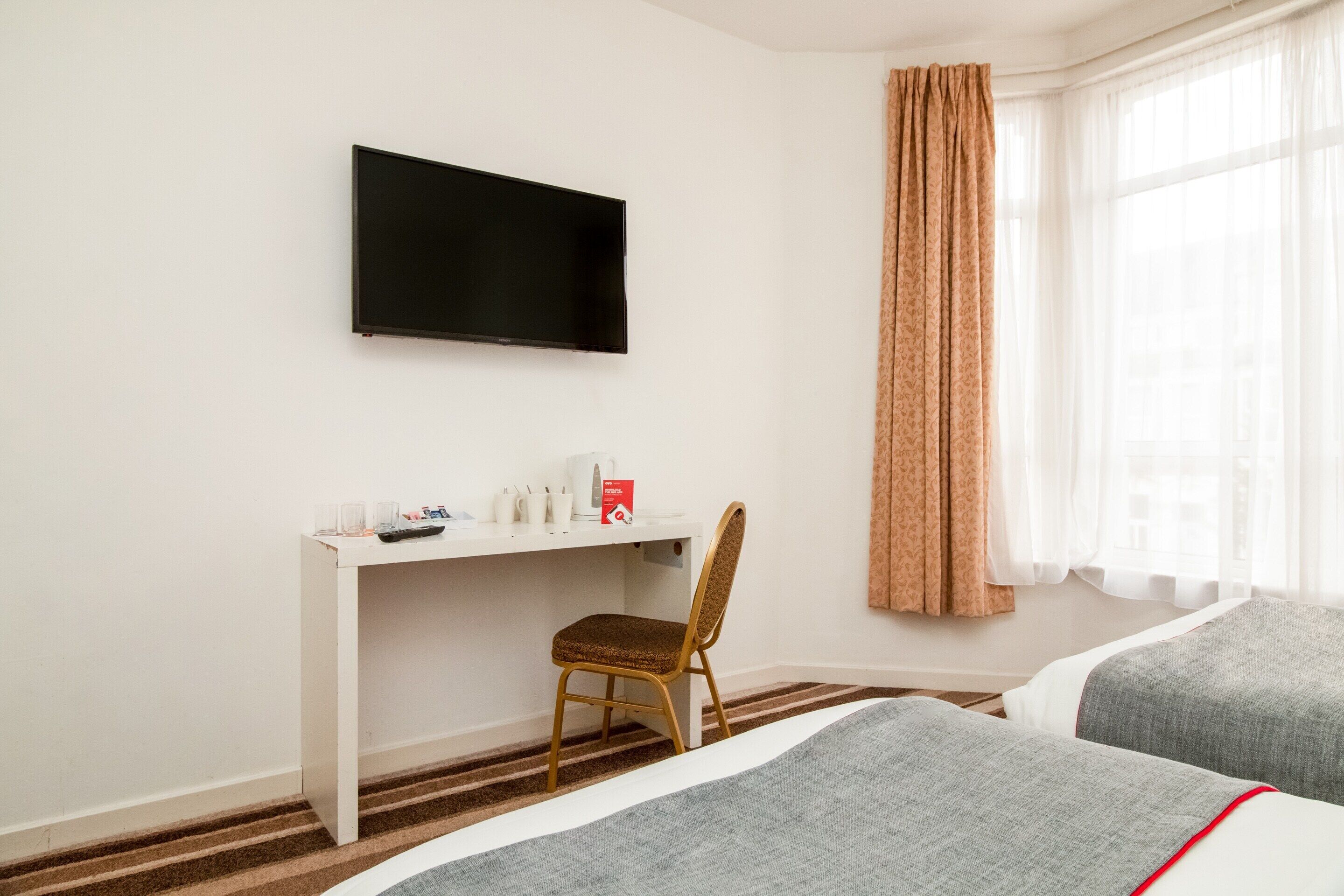 Una habitación de hotel con una cama, un escritorio con silla, televisión y ventana con cortinas.