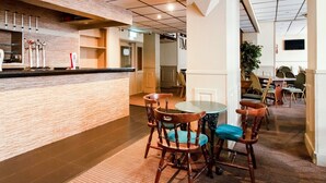 A modern hotel lobby with a wooden reception desk, a round dining table with chairs, and a large potted plant. - Cardiff Riverside Hotel by Belvilla (Cardiff)
