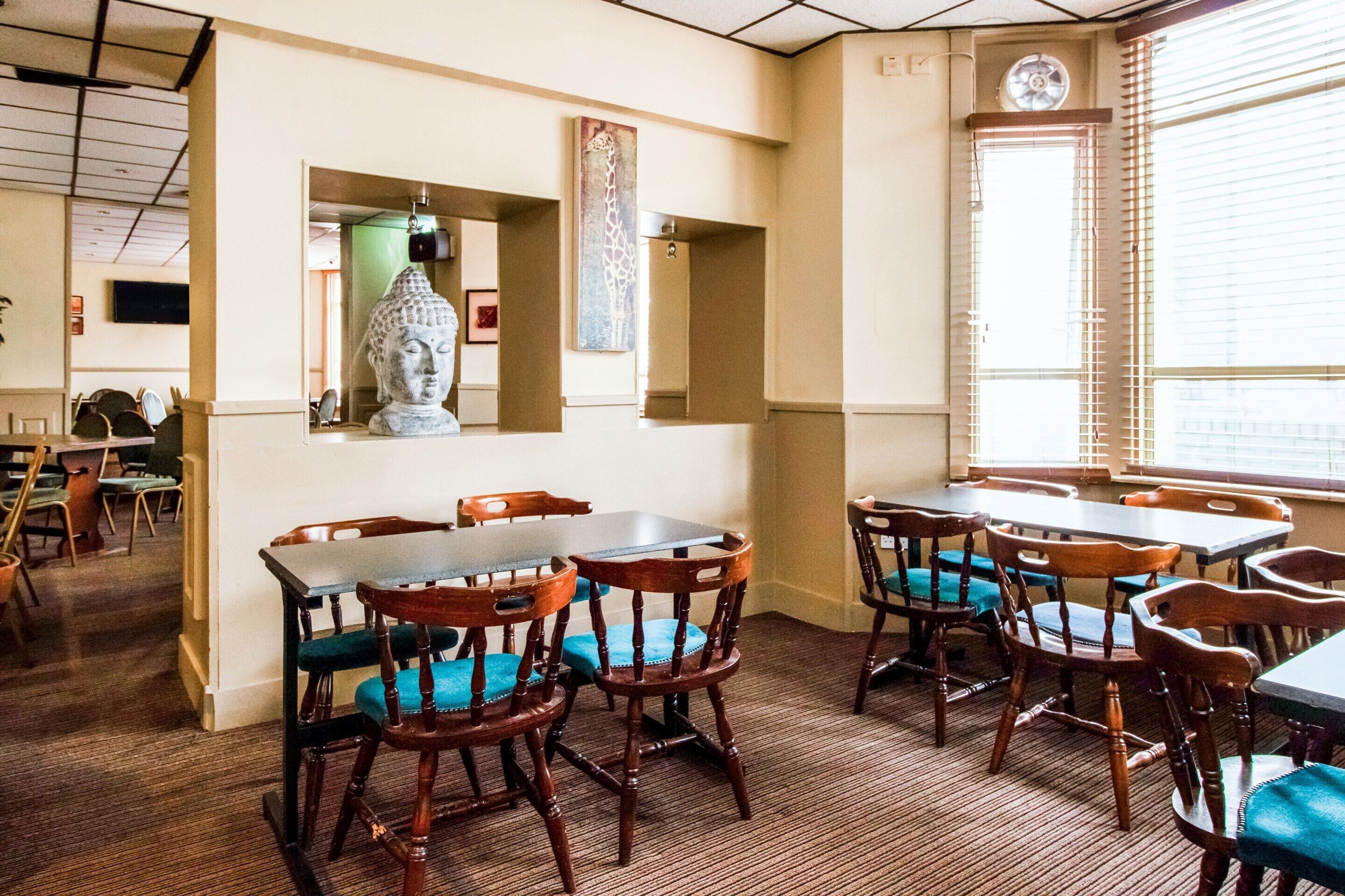 A dining area with wooden tables and chairs, a Buddha statue, and a giraffe painting on the wall.