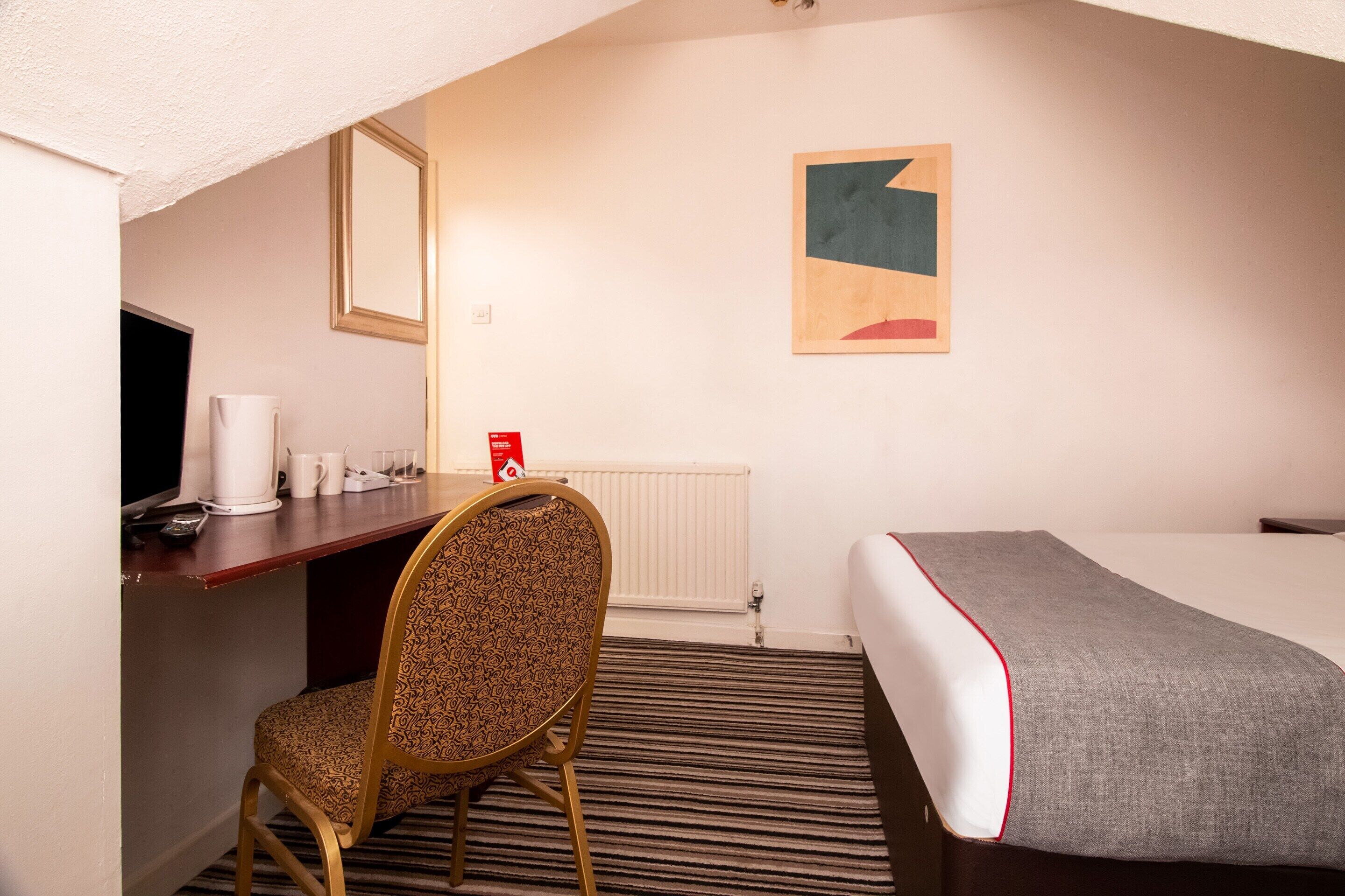 Una habitación de hotel con cama, escritorio, silla, televisor y radiador.
