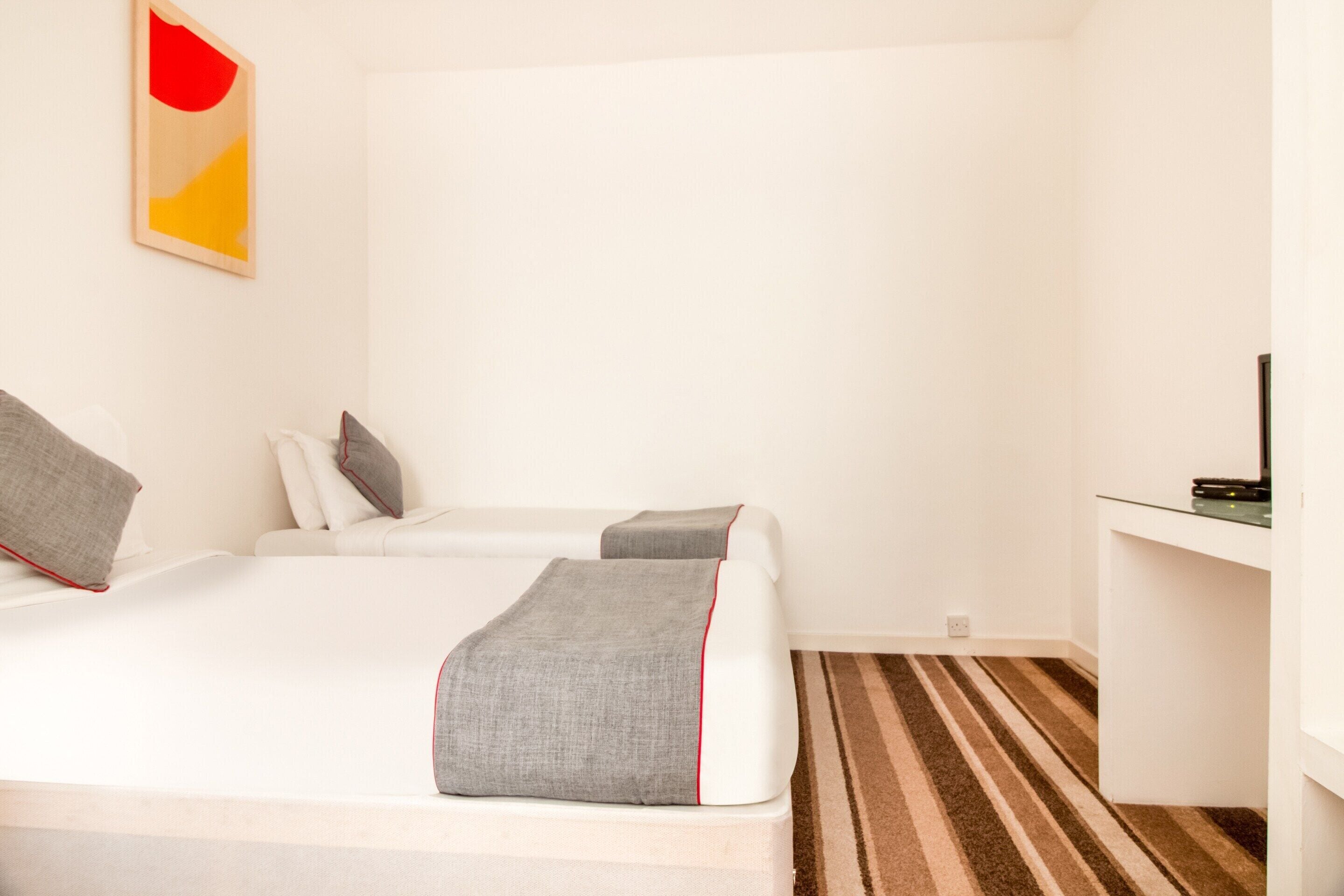 A hotel room with two beds, a TV, a small desk, and a striped carpet.