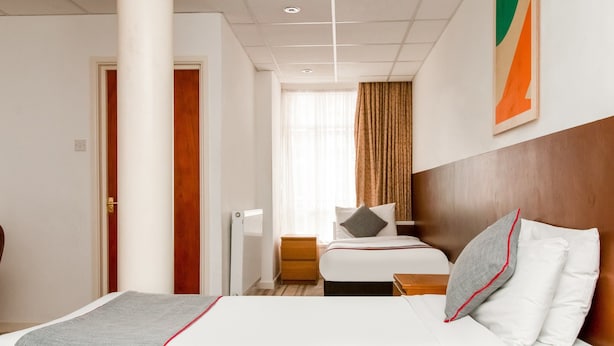 A hotel room with a large bed, a smaller bed, a nightstand, a wooden headboard, a window with curtains, and a wall-mounted artwork. - Cardiff Riverside Hotel by Belvilla (Cardiff)