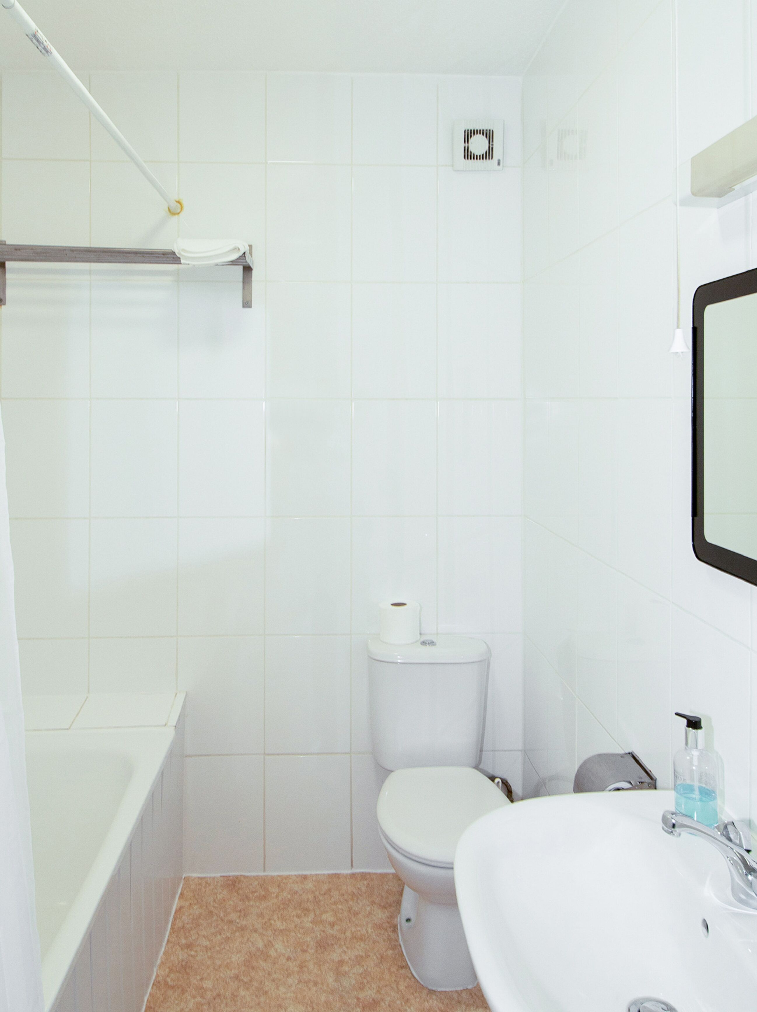 Un baño pequeño y blanco con inodoro, lavamanos y ducha.