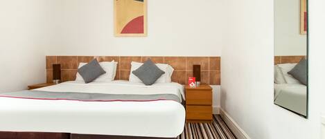 A hotel room with a bed, a nightstand, a mirror, and a wall-mounted artwork.