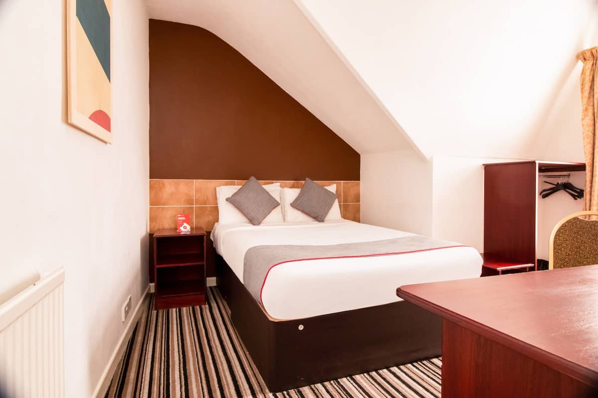A hotel room with a bed, a nightstand, a wooden desk, and a wardrobe.