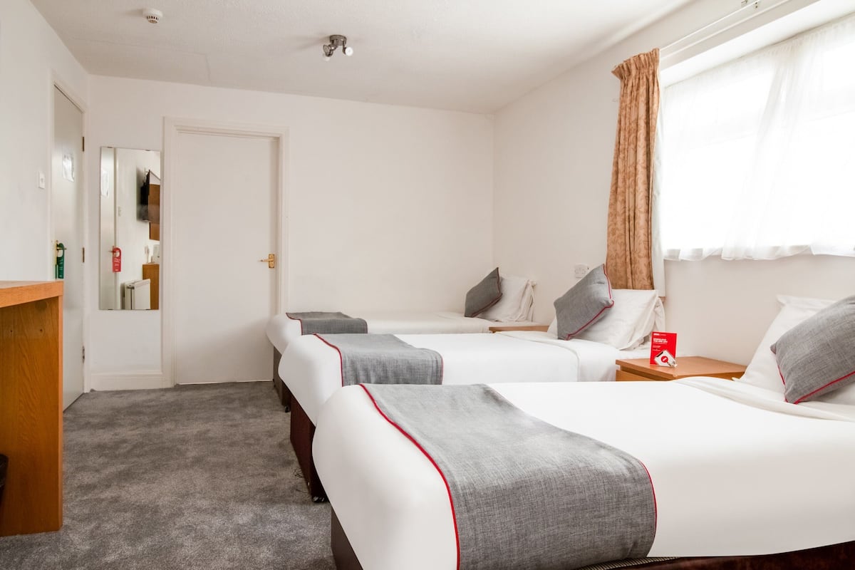 A hotel room with two beds, a wooden desk, a mirror, and a window with curtains.