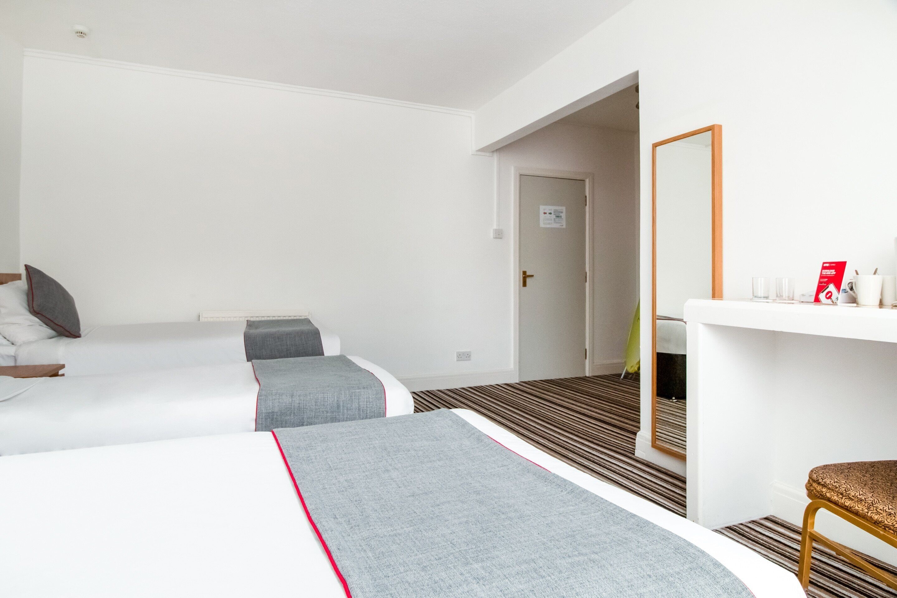 A hotel room with two beds, a small sitting area with a chair, a mirror, and a counter with toiletries.