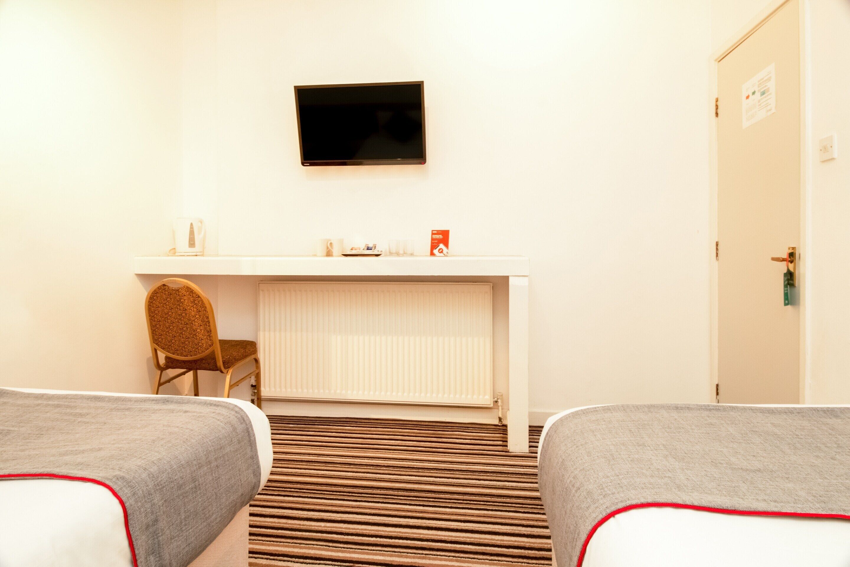 Una habitación de hotel con dos camas, un escritorio, una silla, un televisor y una puerta.