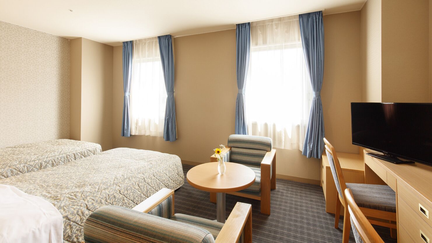 Quarto de hotel com uma cama grande, televisão, mesa pequena com um vaso e duas cadeiras.