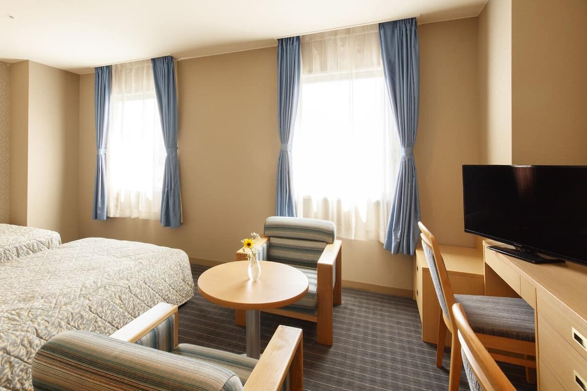 Ein Hotelzimmer mit einem großen Bett, einem Fernseher, einem kleinen Tisch mit einer Vase und zwei Stühlen.