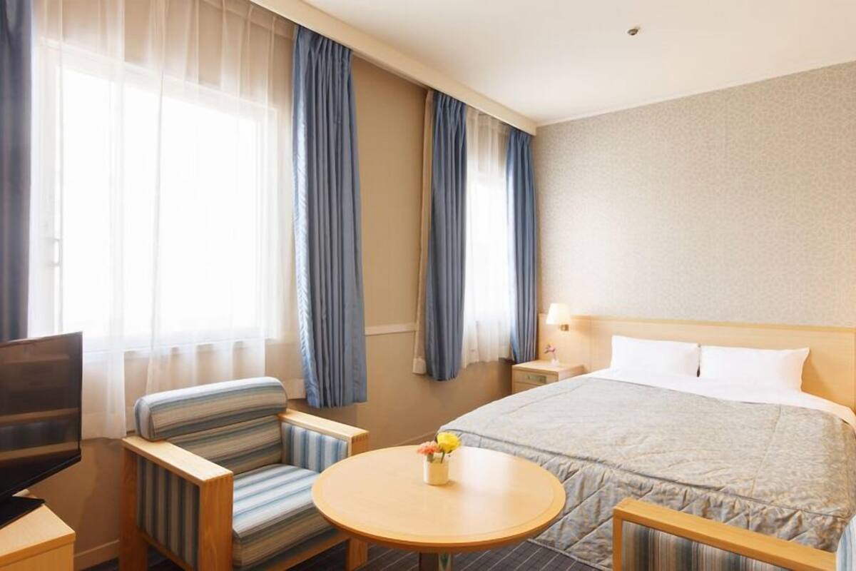 Ein Hotelzimmer mit Bett, Fernseher, Schreibtisch, Stuhl und einem kleinen Tisch mit Blumen.
