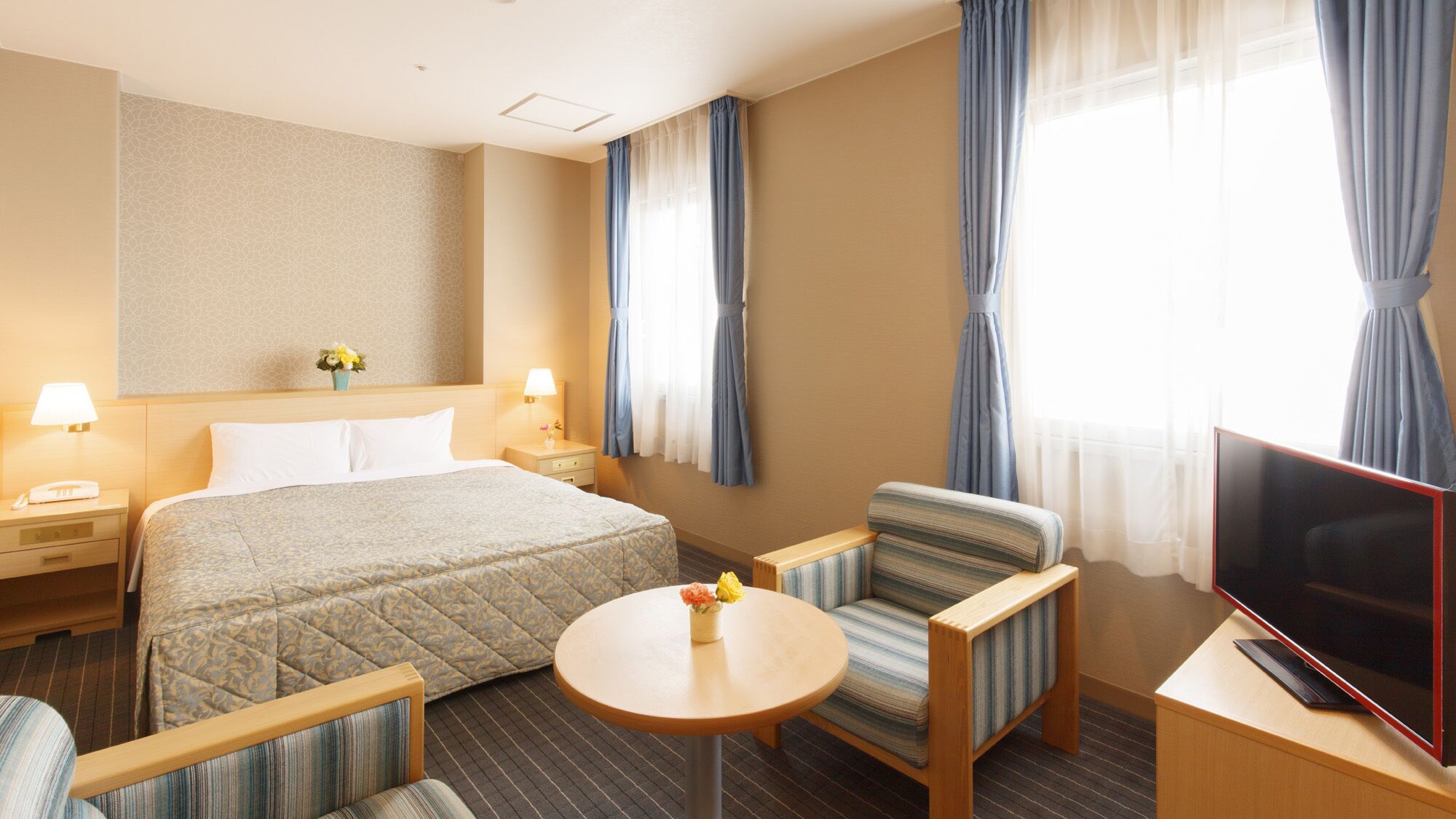 Quarto de hotel com uma cama, duas mesas de cabeceira, uma televisão, uma mesa redonda e duas poltronas.