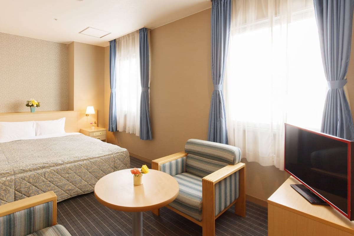 Ein Hotelzimmer mit einem Bett, zwei Nachttischen, einem Fernseher, einem runden Tisch und zwei Sesseln.