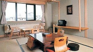 A room with a wooden dining table, chairs, a television on a stand, and a window with curtains. - Hosonokan (Hakuba)