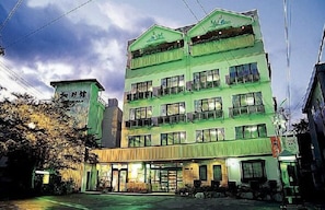 A multi-story building with a green facade, multiple windows, and a visible entrance with a sign.