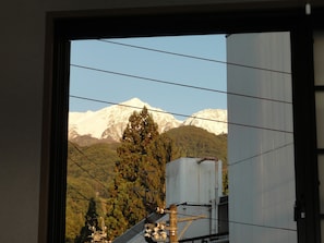 A view through a window of a mountainous landscape with a snow-capped peak, a tree, and industrial structures.