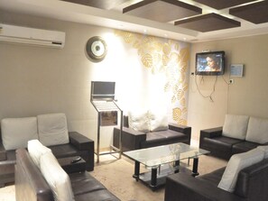 A living room with a sofa, a coffee table, a TV, and a wall-mounted air conditioner. - Hotel Deviram Palace (Agra)