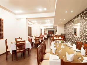 A spacious dining area with multiple tables and chairs, a high ceiling with recessed lighting, and a patterned wall on one side. - Hotel Deviram Palace (Agra)