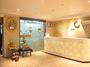 A reception area with a Christmas tree, a clock, and a sign indicating the reception desk. - Hotel Deviram Palace (Agra)