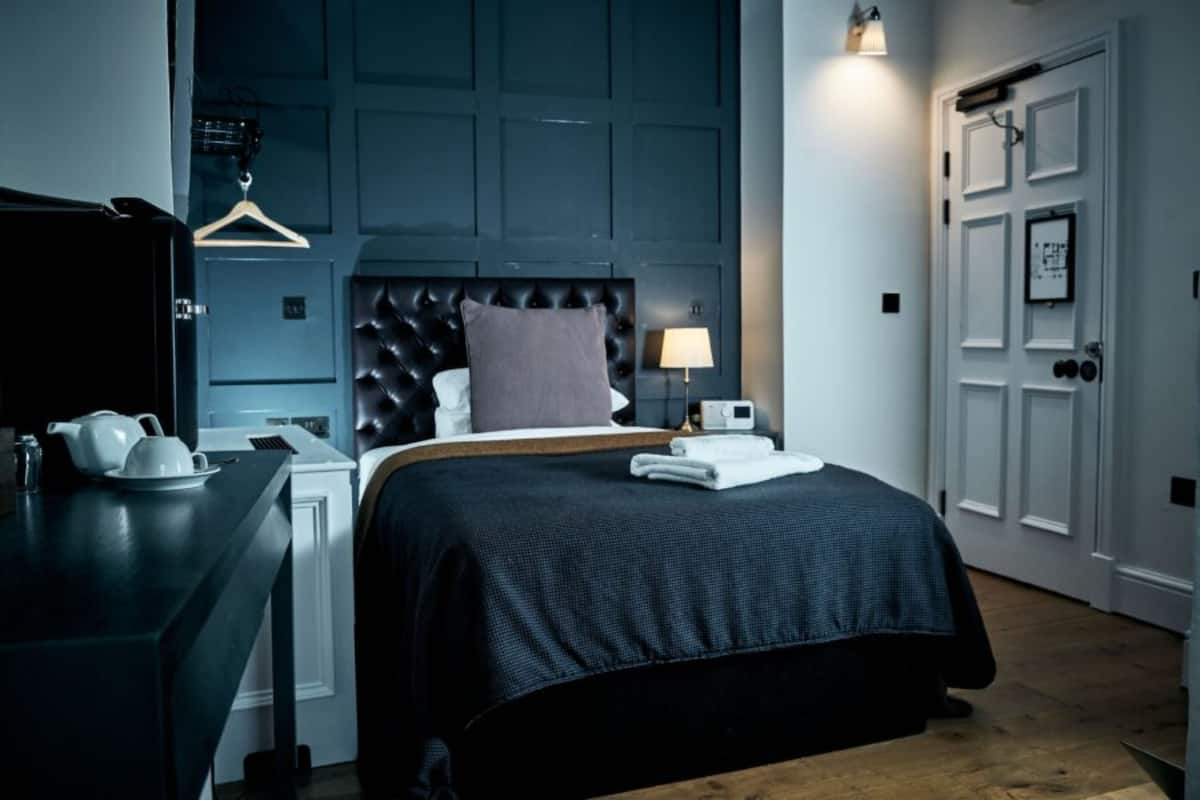 A bedroom with a dark blue headboard, a bedside table with a lamp, and a neatly made bed.