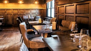 Um restaurante com paredes revestidas de madeira, assentos de couro e mesas preparadas para refeições.