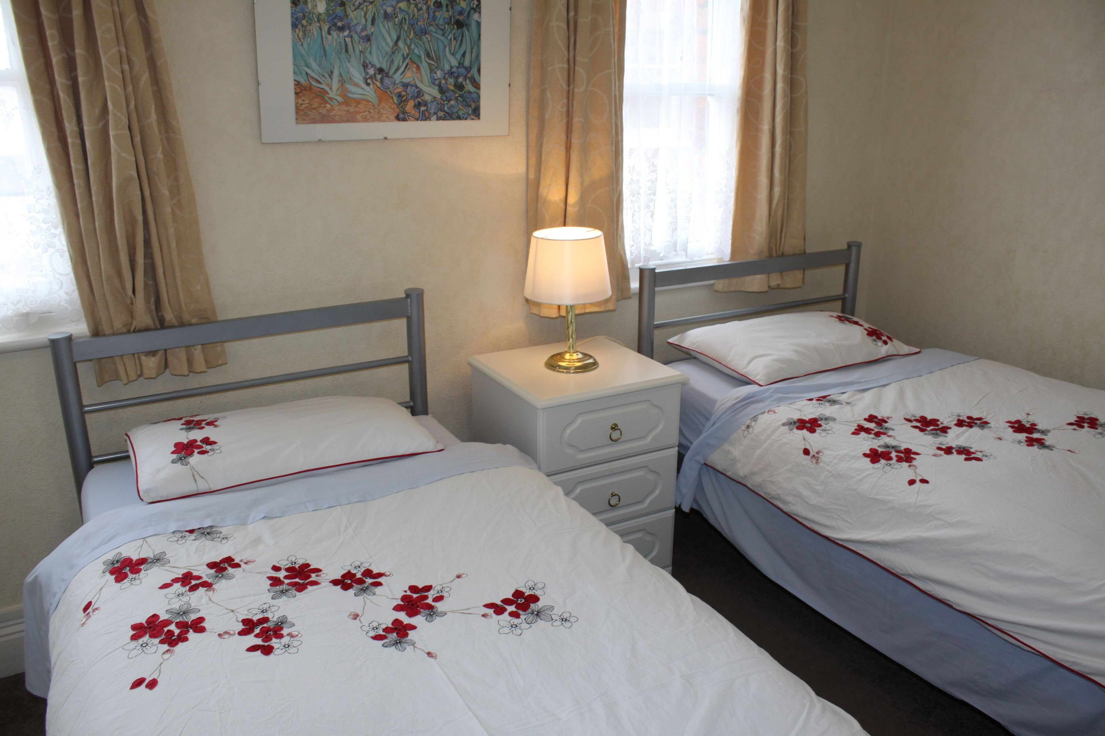 Two single beds with floral bedding, a bedside table with a lamp, and a painting on the wall.