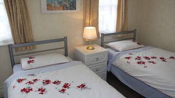 Two single beds with floral bedding, a bedside table with a lamp, and a painting on the wall.