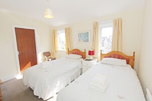 Habitación de hotel con dos camas, cabecera de madera, mesita de noche con lámpara, una silla y una puerta.