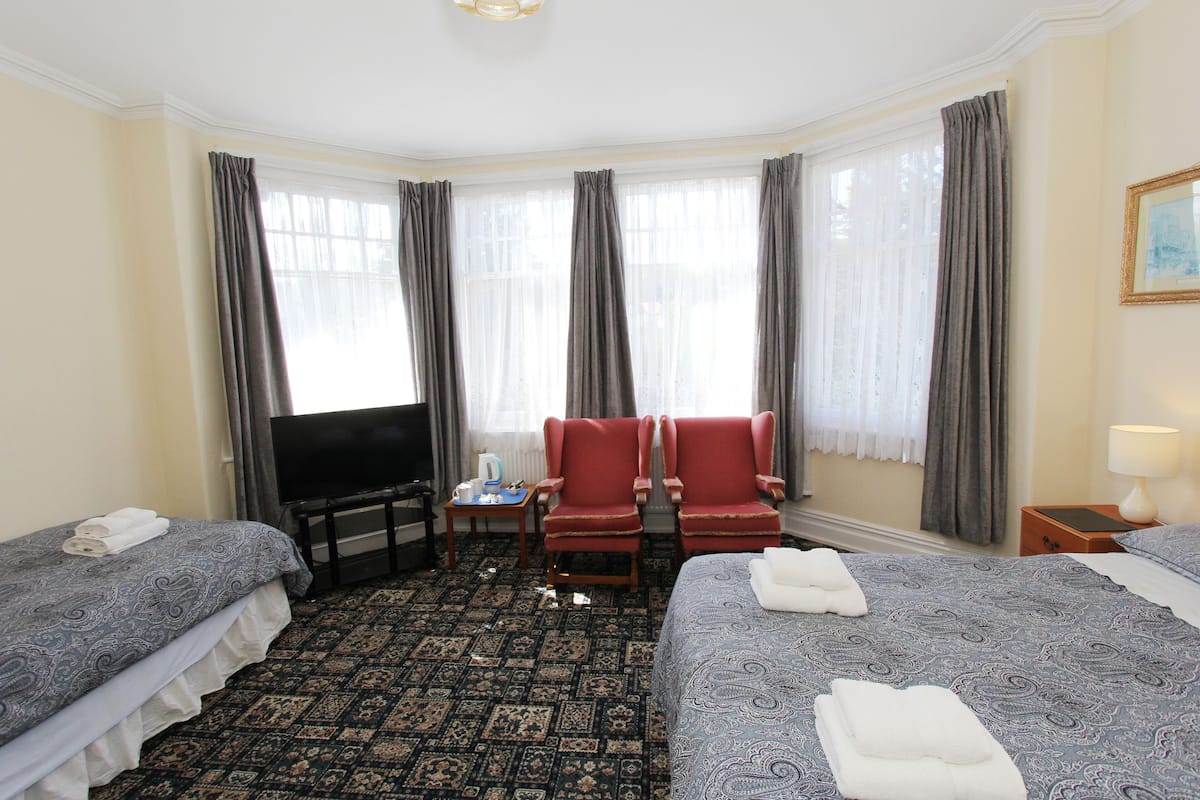 A hotel room with two beds, a television, a small table, two red armchairs, and a window with curtains.