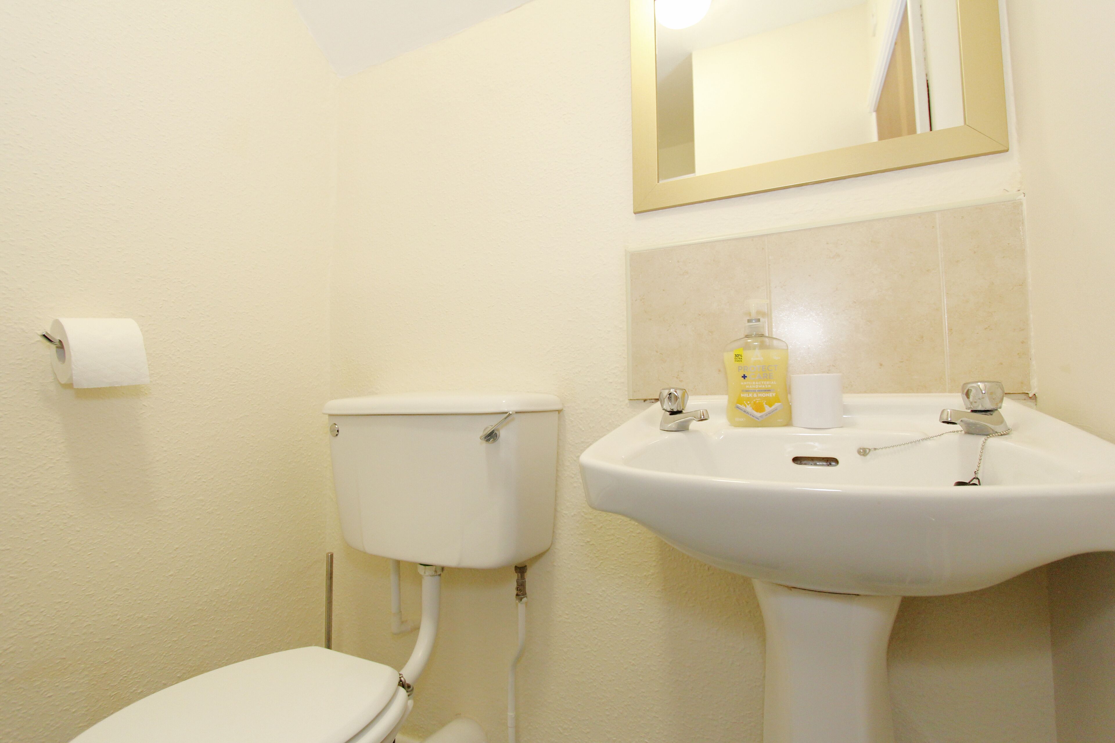 A bathroom with a toilet, sink, and mirror.