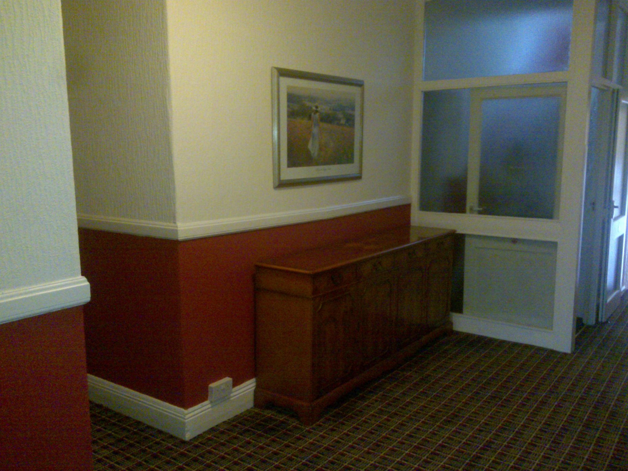 A hallway with a wooden bench, a framed picture on the wall, and a door with frosted glass panels.