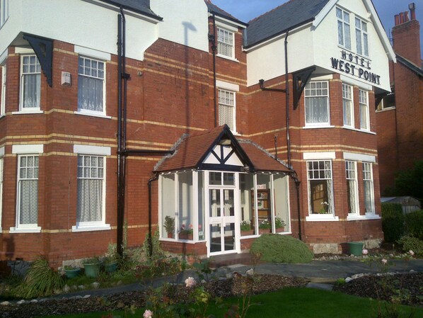 A two-story hotel with a traditional design, featuring a prominent entrance with a small porch and potted plants.