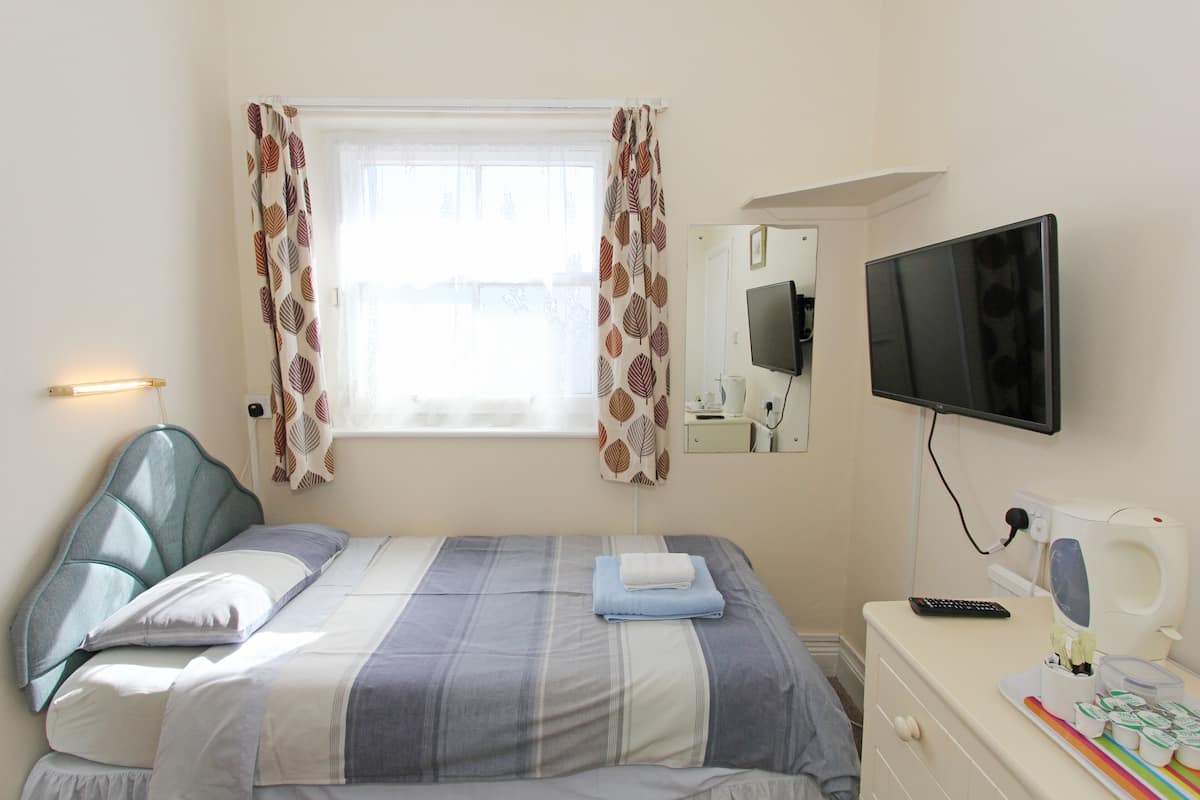 A bedroom with a bed, a television, a bedside table with a remote, and a window with curtains.