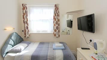 Ein Schlafzimmer mit einem Bett, einem Fernseher, einem Nachttisch mit Fernbedienung und einem Fenster mit Vorhängen.