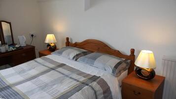 Una cama doble bien hecha con una colcha a rayas, dos lámparas de noche, una mesita de noche de madera y un aparador con espejo y cafetera.