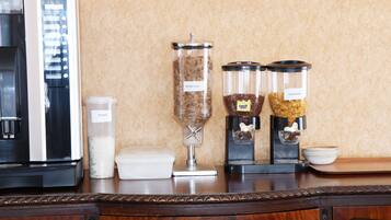 Un coin cuisine avec une machine à café, un récipient étiqueté « muesli », et deux autres récipients étiquetés « branflakes » et « coco pops ».
