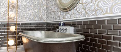 A bathroom with a freestanding bathtub, a gold floor lamp, and a patterned wall.