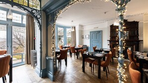 A dining area with tables and chairs, a view through a window, and a decorative archway. - Escape Boutique B&B (Llandudno)