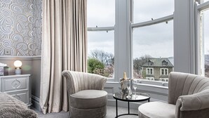 A modern room with a large window, two armchairs, a small round table, and a nightstand with a lamp. - Escape Boutique B&B (Llandudno)