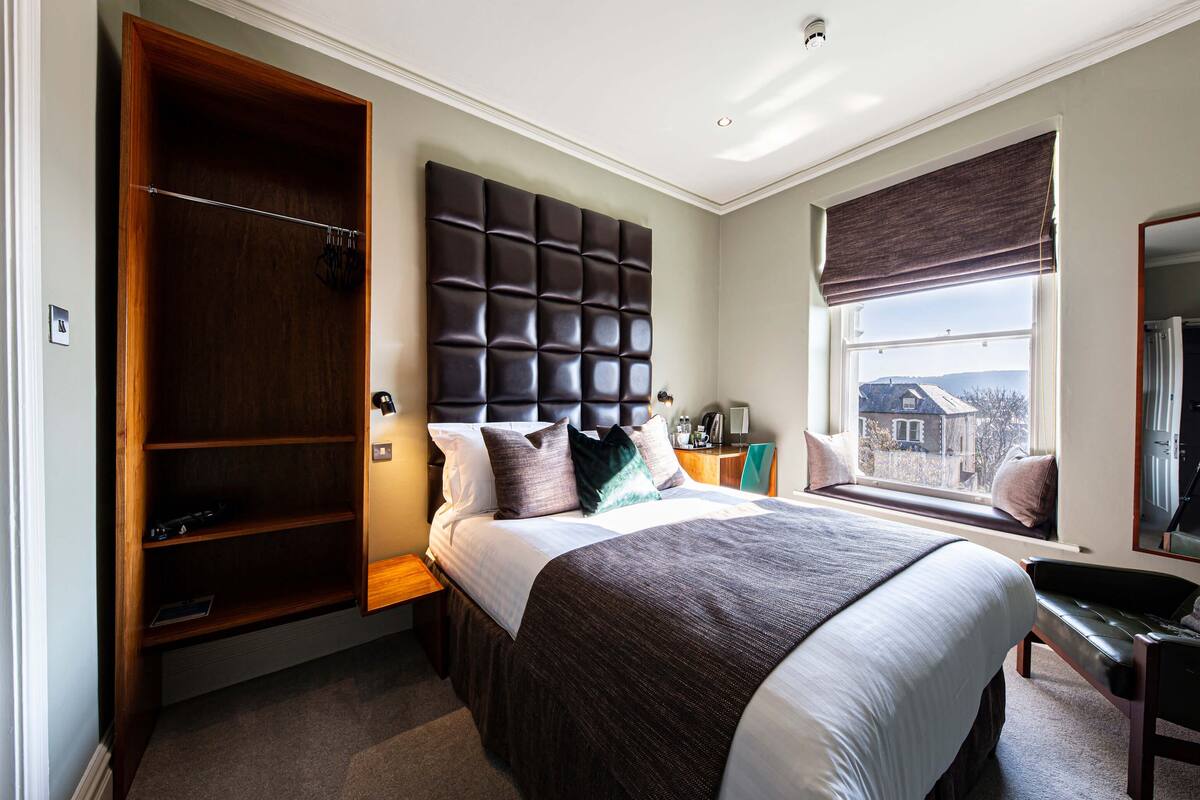 A bedroom with a large bed, a built-in wardrobe, a window with a view, and a bench by the window.