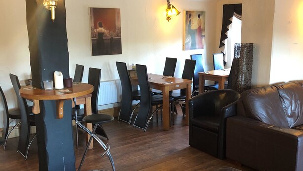 Zona pranzo con tavoli e sedie in legno, un divano e un grande specchio.