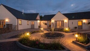 A building with multiple rooms, a central courtyard with a circular flower bed, and outdoor seating. - Canaston Oaks (Narberth)