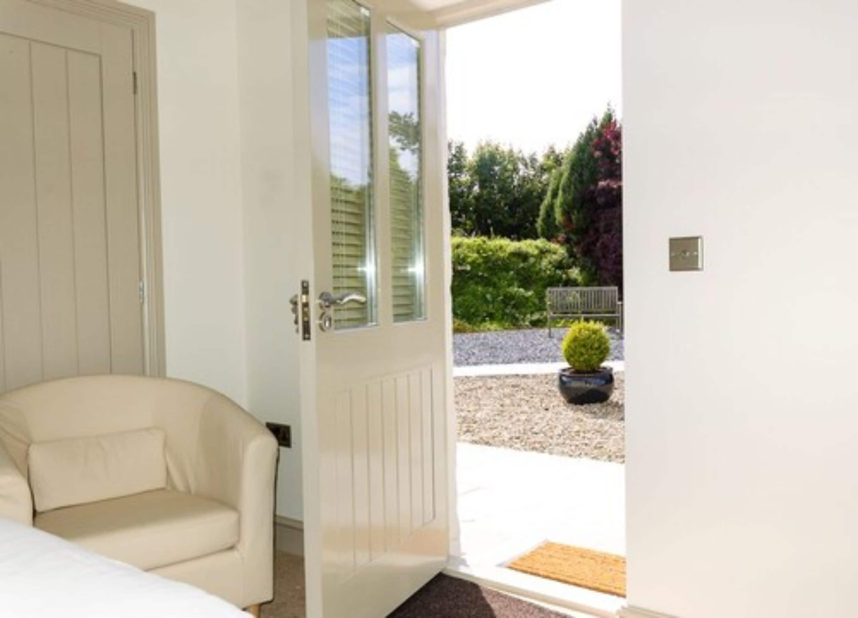 A room with a beige sofa, a white door leading outside, and a small potted plant on the patio.