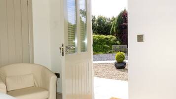 A room with a beige sofa, a white door leading outside, and a small potted plant on the patio.