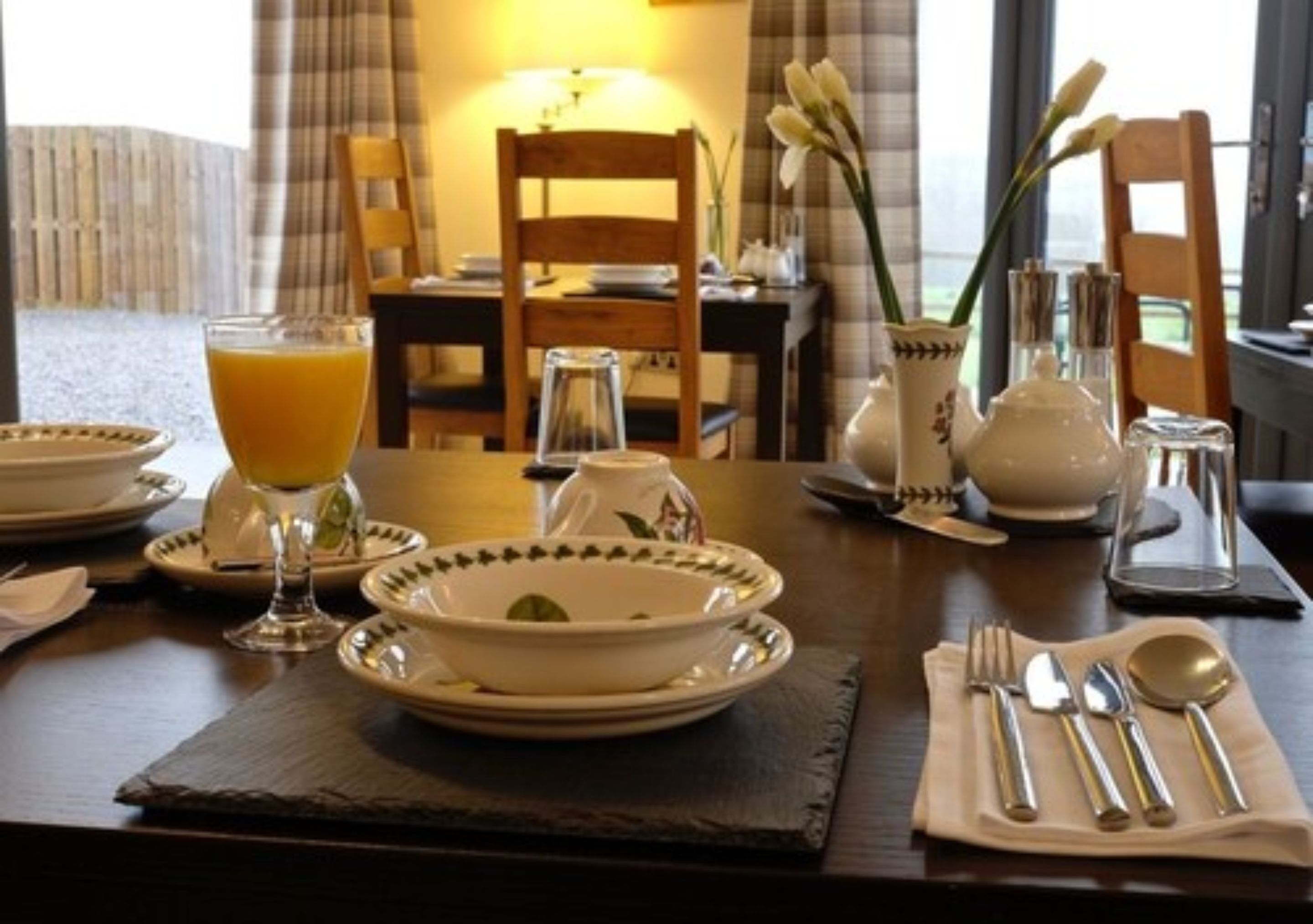 Una mesa de comedor dispuesta con platos, cuencos, un vaso de jugo de naranja y cubiertos.