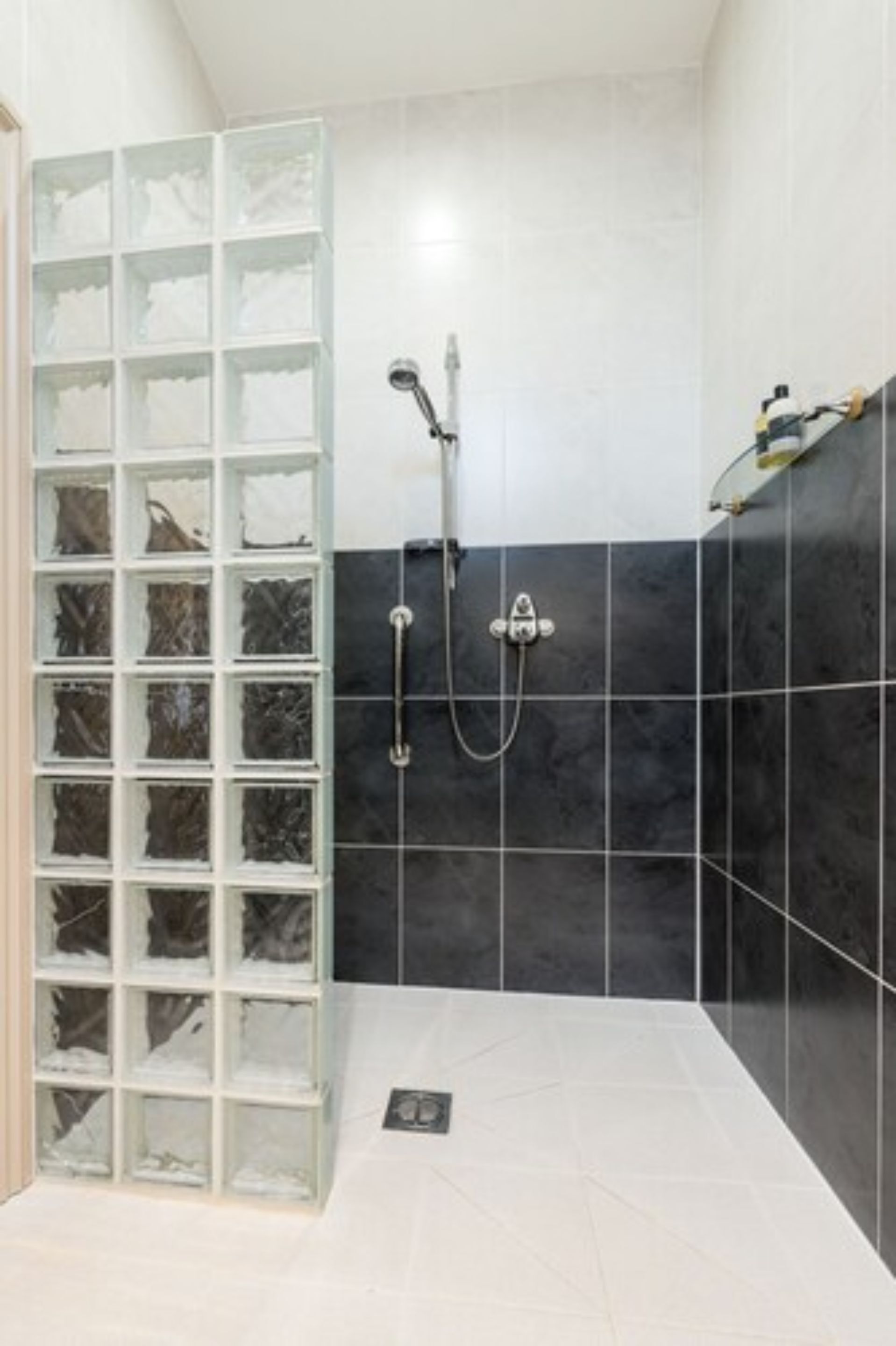 A bathroom with a glass shower enclosure, a handheld showerhead, and a wall-mounted faucet.