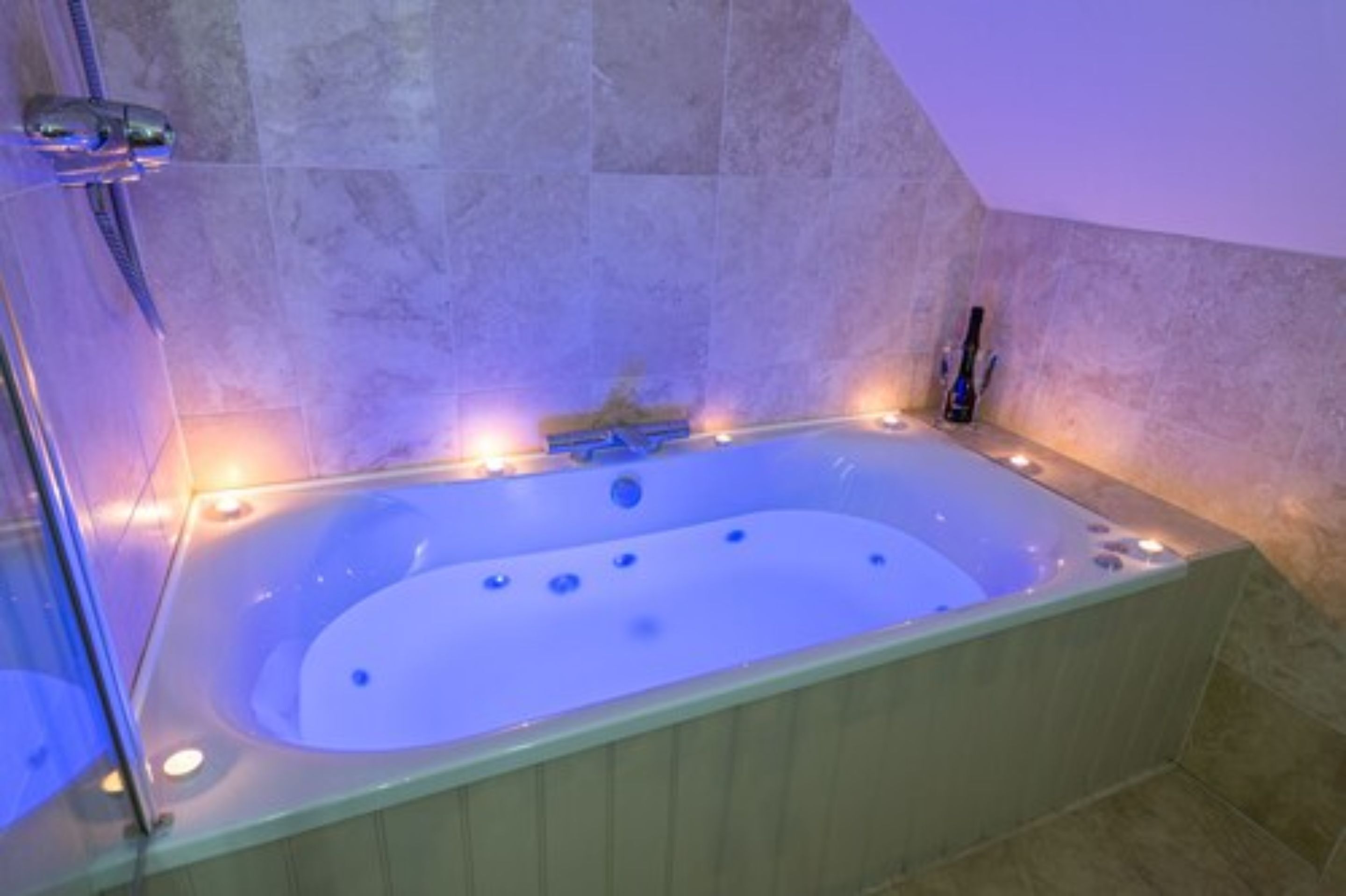 A large, rectangular hot tub with a built-in seat, surrounded by stone walls and a glass enclosure.